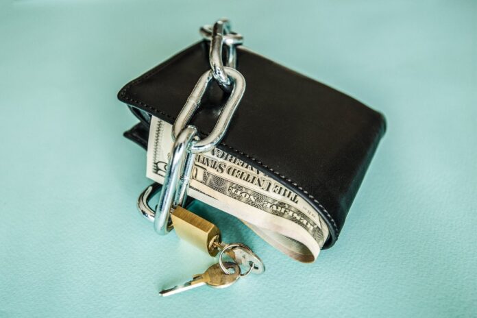 A wallet full of money is locked up with a chain and a padlock.