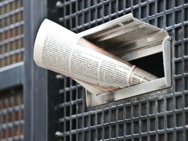 A newspaper stuck into the mail slot on a residential door - Newsbyte Concept